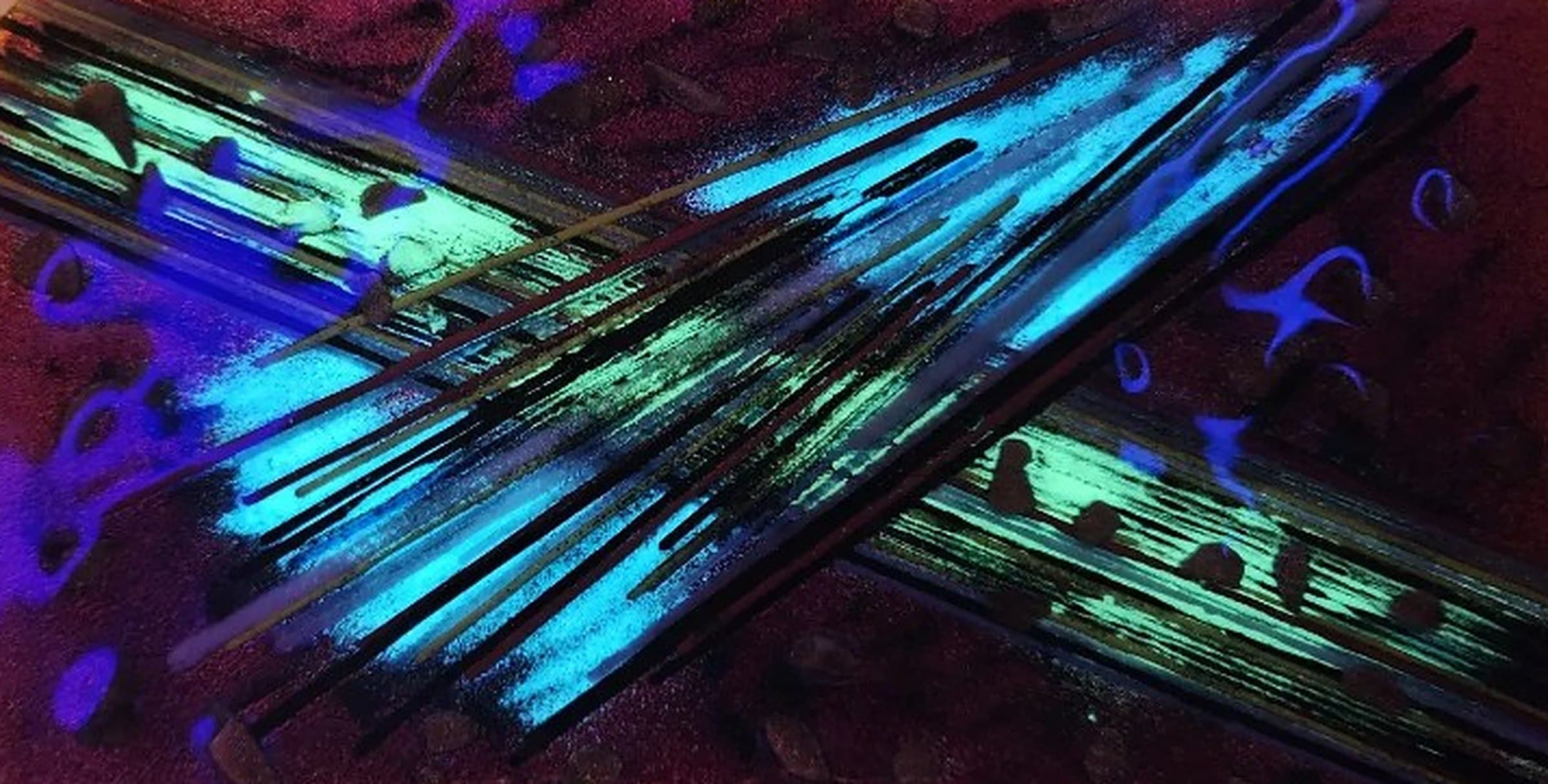Fused glass panel glowing turquoise, green and violet under blacklight, with dark streaks crossing a deep red surface